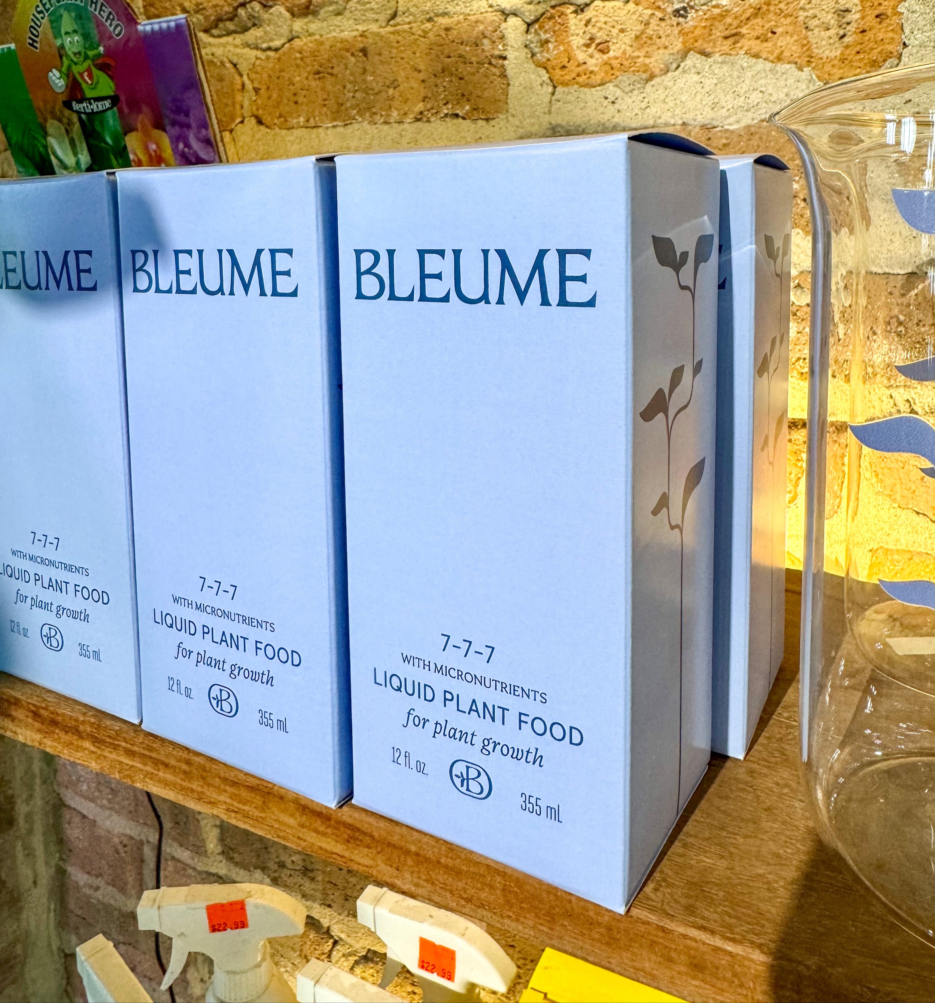 Bleume liquid plant food boxes on a wooden shelf with a stone wall background